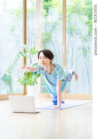 Middle-aged woman doing online yoga in the living room 90163950