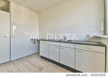 Fragment of interior of light narrow home kitchen with minimalist style white furniture with sink and stove Fragment of interior of light narrow home kitchen with minimalist style white furniture with sink and stove 90163958