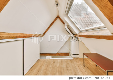 A small room on the top floor of a residential house with a triangular roof and appropriate furniture A small room on the top floor of a residential house with a triangular roof and appropriate furniture 90164054