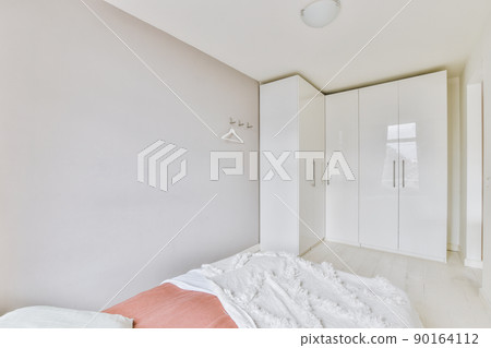 Home interior design of bedroom with bed and wooden wardrobe placed in corner near window in modern apartment 90164112