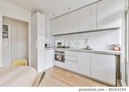 Fragment of interior of light narrow home kitchen with minimalist style white furniture with sink and stove Fragment of interior of light narrow home kitchen with minimalist style white furniture with sink and stove 90164294