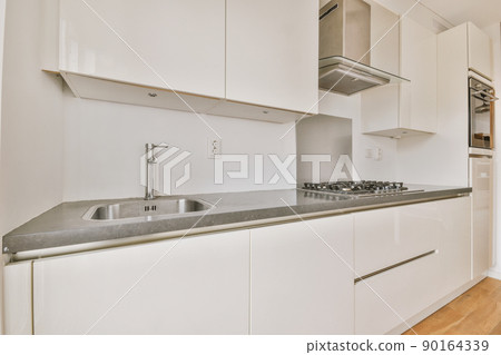 Fragment of interior of light narrow home kitchen with minimalist style white furniture with sink and stove Fragment of interior of light narrow home kitchen with minimalist style white furniture with sink and stove 90164339