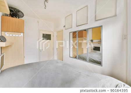 A bedroom with a large gray bed and several mirrors in a cozy modern apartment A bedroom with a large gray bed and several mirrors in a cozy modern apartment 90164395