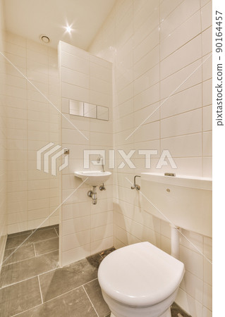 Modern flush toilet and ceramic sink installed on white tiled walls near mirror and towel in small restroom at home Modern flush toilet and ceramic sink installed on white tiled walls near mirror and towel in small restroom at home 90164457