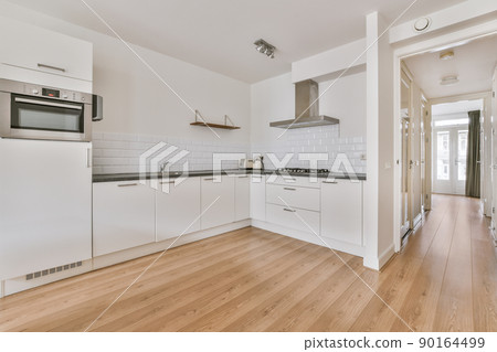 Fragment of interior of light narrow home kitchen with minimalist style white furniture with sink and stove 90164499
