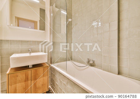 A cozy bathroom with a ceramic sink and a bathtub with a glazed shower in a modern house A cozy bathroom with a ceramic sink and a bathtub with a glazed shower in a modern house 90164788