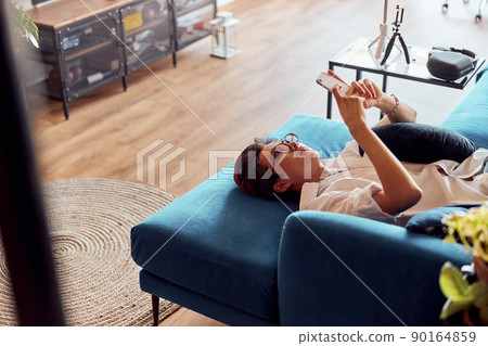 Relaxed Asian guy using a smart phone lying on an couch 90164859