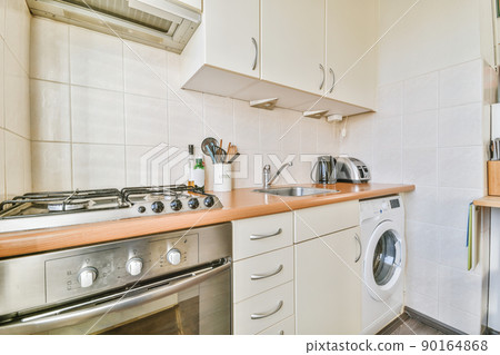 Fragment of interior of light narrow home kitchen with minimalist style white furniture with sink and stove 90164868