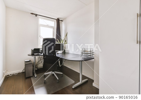 Comfortable chair placed near desk with computer monitor located close to small window in light workplace in modern apartment Comfortable chair placed near desk with computer monitor located close to small window in light workplace in modern apartment 90165016