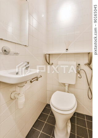 Wall hung toilet and small sink in corner in lavatory room with beige tile 90165045