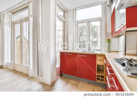 Small corner kitchen with sink under window and red furniture with transparent cupboards with stove near balcony Small corner kitchen with sink under window and red furniture with transparent cupboards with stove near balcony 90165694
