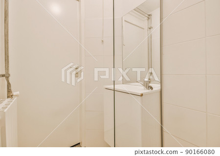 Sink with tap under the mirror placed against radiator in white tiled restroom at home Sink with tap under the mirror placed against radiator in white tiled restroom at home 90166080