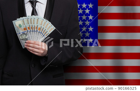 American man hand with 100 US dollar bills money banknotes against flag of USA country background 90166325