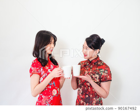 Portrait of mature asian mother and her asian daughter both wearing traditional cheongsam qipao dress relaxing drinking on white background. Portrait of mature asian mother and her asian daughter both wearing traditional cheongsam qipao dress relaxing drinking on white background. 90167492