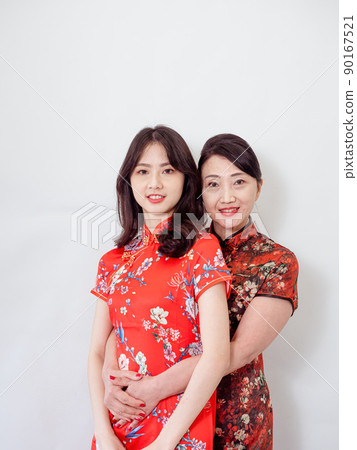 Portrait of mature asian mother hugging with her asian daughter on white background(Both wearing traditional cheongsam qipao). Portrait of mature asian mother hugging with her asian daughter on white background(Both wearing traditional cheongsam qipao). 90167521