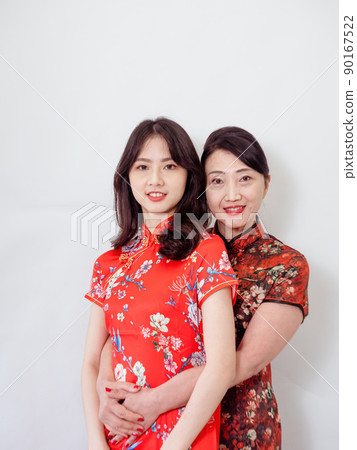 Portrait of mature asian mother hugging with her asian daughter on white background(Both wearing traditional cheongsam qipao). Portrait of mature asian mother hugging with her asian daughter on white background(Both wearing traditional cheongsam qipao). 90167522
