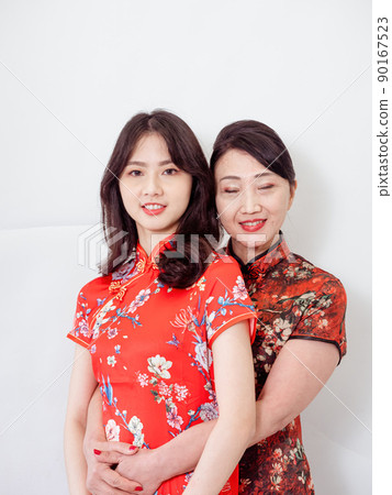 Portrait of mature asian mother hugging with her asian daughter on white background(Both wearing traditional cheongsam qipao). Portrait of mature asian mother hugging with her asian daughter on white background(Both wearing traditional cheongsam qipao). 90167523