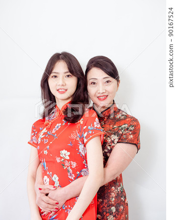 Portrait of mature asian mother hugging with her asian daughter on white background(Both wearing traditional cheongsam qipao). Portrait of mature asian mother hugging with her asian daughter on white background(Both wearing traditional cheongsam qipao). 90167524