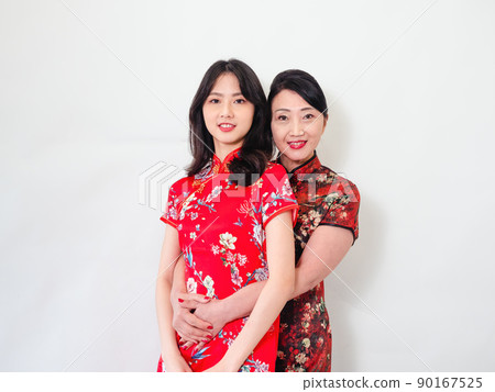 Portrait of mature asian mother hugging with her asian daughter on white background(Both wearing traditional cheongsam qipao). Portrait of mature asian mother hugging with her asian daughter on white background(Both wearing traditional cheongsam qipao). 90167525