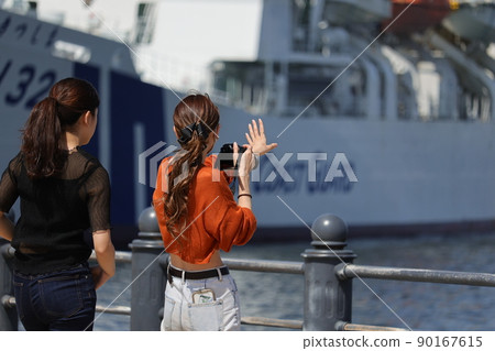 Two women taking pictures of a ship at the harbor 90167615