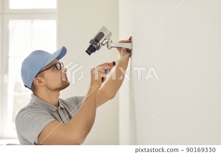 Professional male surveillance camera installer mounts it on wall inside new home or office. 90169330