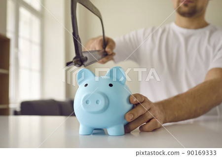 Strange young man needs money and is going to cut through his piggy bank with a saw Strange young man needs money and is going to cut through his piggy bank with a saw 90169333
