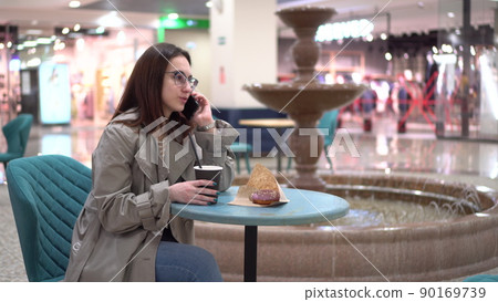 A young woman in a cafe speaks on the phone against the background of a fountain. Decoration in the cafe. 90169739