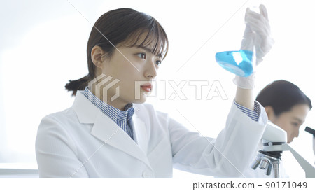 A woman in a white coat staring at a flask Research experiment 90171049