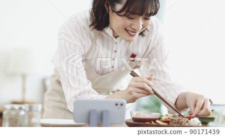 A young woman cooking while looking at her smartphone A young woman cooking while looking at her smartphone 90171439