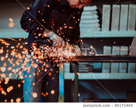 Heavy Industry Engineering Factory Interior with Industrial Worker Using Angle Grinder and Cutting a Metal Tube. Contractor in Safety Uniform and Hard Hat Manufacturing Metal Structures. 90172404