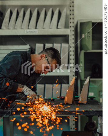 Heavy Industry Engineering Factory Interior with Industrial Worker Using Angle Grinder and Cutting a Metal Tube. Contractor in Safety Uniform and Hard Hat Manufacturing Metal Structures. Heavy Industry Engineering Factory Interior with Industrial Worker Using Angle Grinder and Cutting a Metal Tube. Contractor in Safety Uniform and Hard Hat Manufacturing Metal Structures. 90172409