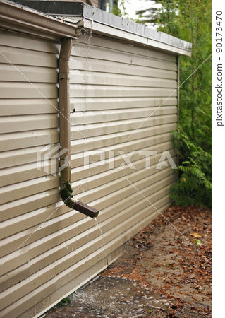 Rain Water Pours Out of a Short Downspout on side of house pooling by foundation 90173470