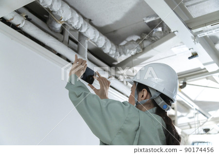 Female air conditioning equipment engineer shooting with a smartphone Female air conditioning equipment engineer shooting with a smartphone 90174456