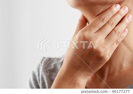 sore throat pain. Closeup of young woman sick holding her inflamed throat using hands to touch the ill neck in blue shirt on gray background. Medical and healthcare concept. Focus red on to show pain. 90177277