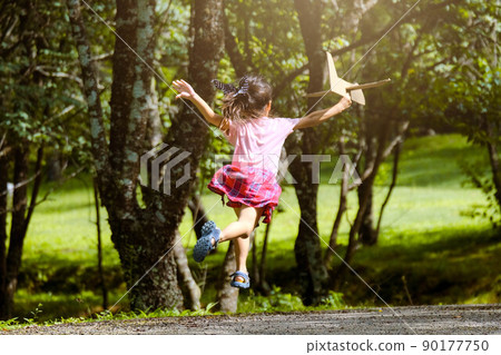 Happy little girl playing with airplanes made of cardboard in summer park. Cute girl with a toy airplane running on the road in the park. Happy childhood concept. Happy little girl playing with airplanes made of cardboard in summer park. Cute girl with a toy airplane running on the road in the park. Happy childhood concept. 90177750