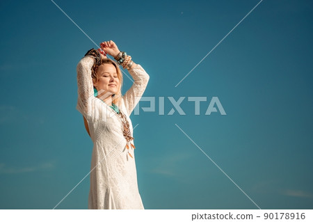 Woman in bohemian clothing on beach at sunset. Boho style for fashionable look on resort. Middle aged well looking woman in white dress and boho style braclets. Summer fashion 90178916