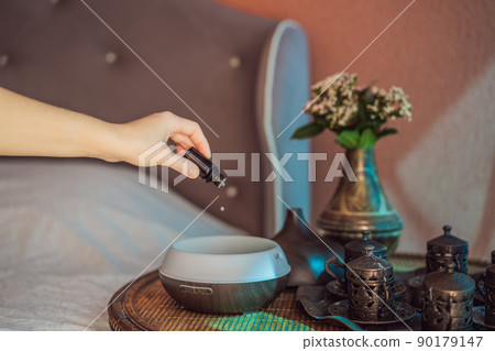 Woman adding essential oil to aroma diffuser on table 90179147