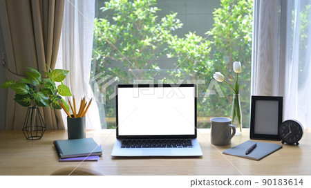 Front view laptop computer with blank screen, houseplant, picture frame and stationery on wooden table 90183614