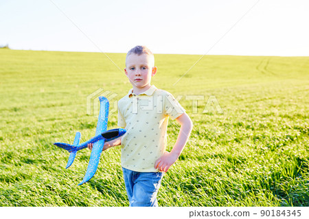 Boy runs with toy airplane in summer through field. Happy child running and playing with toy airplane outdoors. Boy dreams of flying. Carefree child is playing. 90184345