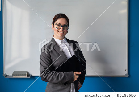 Beautiful woman in a suit with a digital tablet in her hands. A smiling female business coach with glasses stands in a conference room near a white board. Workshop at the office. Beautiful woman in a suit with a digital tablet in her hands. A smiling female business coach with glasses stands in a conference room near a white board. Workshop at the office. 90185690