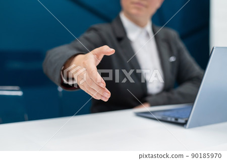 Faceless woman in a business suit holds out her hand for a handshake while sitting at a desk. Female boss makes a successful deal. 90185970