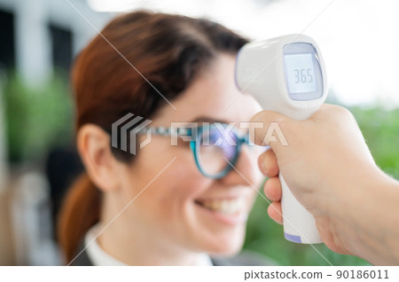 Mandatory measurement of a fever non-contact thermometer gun of all office workers. Happy woman with normal body temperature. Infrared portable device needed during an epidemic. 90186011