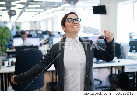 Business woman takes off the mask in the office at the end of quarantine. Coronavirus over time to return to work. The girl breathes freely and smiles. Victory over the pandemic. Return to normal. 90186212