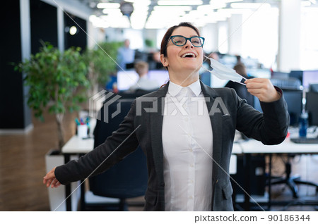 Business woman takes off the mask in the office at the end of quarantine. Coronavirus over time to return to work. The girl breathes freely and smiles. Victory over the pandemic. Return to normal. 90186344