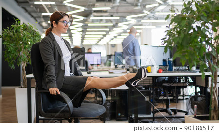 Happy business woman doing abdominal muscle exercises in an open space office. A red-haired smiling female employee in a skirt and high heels is dying off a chair in the workplace. Fitness at work. Happy business woman doing abdominal muscle exercises in an open space office. A red-haired smiling female employee in a skirt and high heels is dying off a chair in the workplace. Fitness at work. 90186517