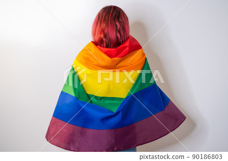 Young red-haired woman stands with her back against a white background and holds the lgbt flag 90186803