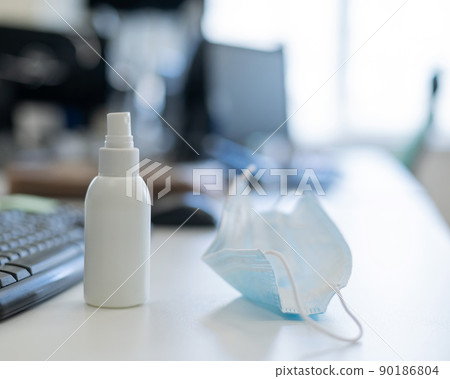 The office manager's desk during the coronavirus epidemic. Medical facial mask and hand antiseptic at the keyboard on a white table. Personal protective equipment against covid-19 for employees. 90186804