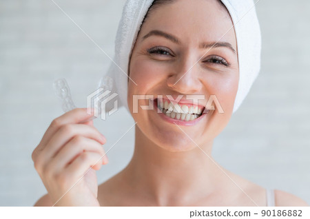 A woman with a towel on her head holds a whitening mouth guard for teeth. The girl aligns her teeth with the help of transparent night removable retainers. Orthodontic device for a perfect smile. 90186882