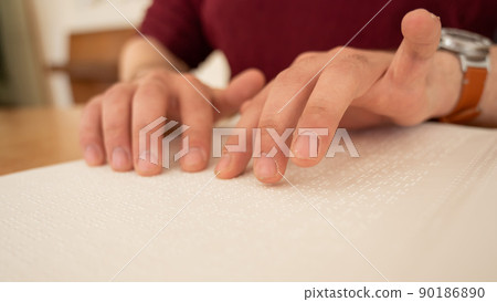 Visually impaired man reading a braille book.  90186890