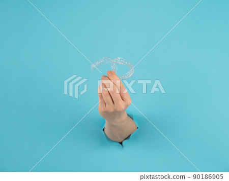 A female hand sticking out of a hole from a blue background holds removable night retainers. A female hand sticking out of a hole from a blue background holds removable night retainers. 90186905